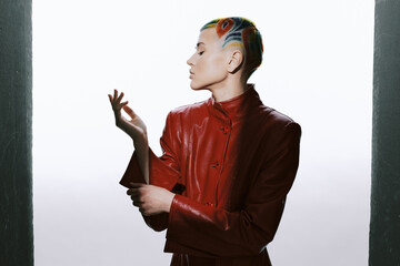 Young woman with artistic short hair and vibrant colors wearing a stylish red leather jacket poses...
