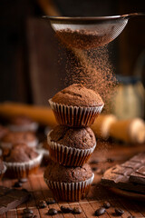 Chocolate muffins with liquid chocolate and dulce de leche with cocoa powder, a chocolate bar, and coffee beans on a wooden table with kitchen utensils.