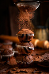 Chocolate muffins with liquid chocolate and dulce de leche with cocoa powder, a chocolate bar, and coffee beans on a wooden table with kitchen utensils.