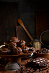 Chocolate muffins with liquid chocolate and dulce de leche with cocoa powder, a chocolate bar, and coffee beans on a wooden table with kitchen utensils.