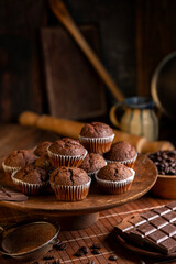 Chocolate muffins with liquid chocolate and dulce de leche with cocoa powder, a chocolate bar, and coffee beans on a wooden table with kitchen utensils.
