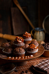 Chocolate muffins with liquid chocolate and dulce de leche with cocoa powder, a chocolate bar, and coffee beans on a wooden table with kitchen utensils.