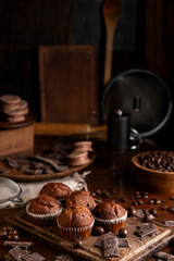 Chocolate muffins with liquid chocolate and dulce de leche with cocoa powder, a chocolate bar, and coffee beans on a wooden table with kitchen utensils.