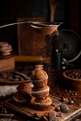 Chocolate muffins with liquid chocolate and dulce de leche with cocoa powder, a chocolate bar, and coffee beans on a wooden table with kitchen utensils.