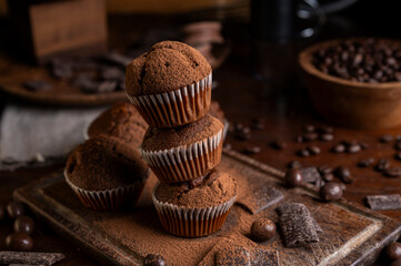 Chocolate muffins with liquid chocolate and dulce de leche with cocoa powder, a chocolate bar, and coffee beans on a wooden table with kitchen utensils.