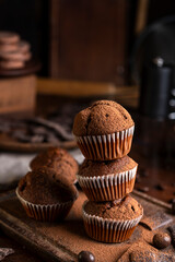 Chocolate muffins with liquid chocolate and dulce de leche with cocoa powder, a chocolate bar, and coffee beans on a wooden table with kitchen utensils.