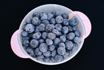 A large bowl brimming with fresh blueberries sits on a dark surface showcasing their vibrant blue color and inviting appearance for healthy eating and culinary uses