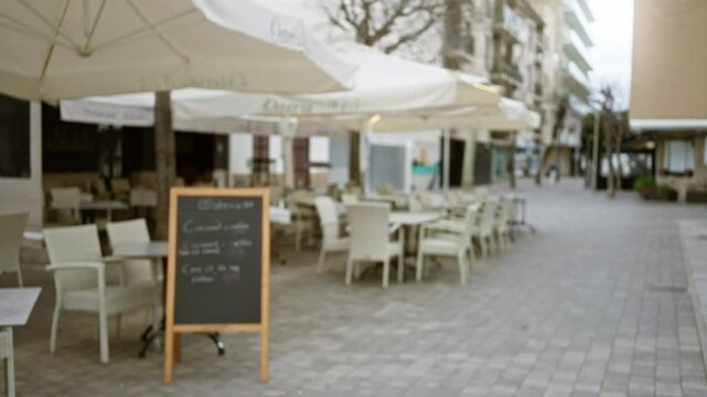Outdoor cafe with chalkboard menu on deserted mediterranean street with blurred tables and chairs under umbrellas, capturing an empty peaceful old town scene.