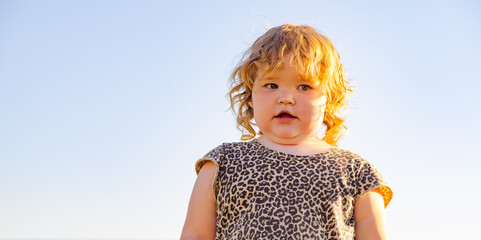 A small child with curly hair stands confidently outside dressed in a leopard print dress The...