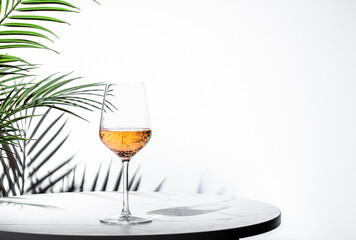 sleek glass of rose pink wine sits elegantly on a marble table, surrounded by lush greenery,...