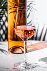 Refreshing rose pink wine in a glass beside an elegant bottle on a marble table adorned with palm...