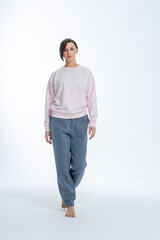 Fototapeta premium Beautiful woman of model appearance. Girl in light pink jumper and gray trousers on light background. Pretty female with trendy makeup posing in studio. Vertical photo. High quality photo
