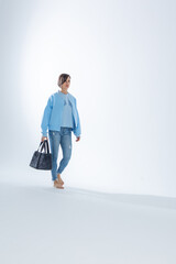 Beautiful woman of model appearance. Girl in blue clothes with black bag on grey background. Pretty...