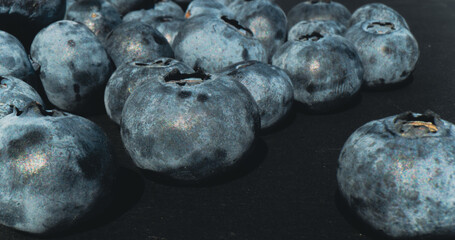 Clusters of freshly collected blueberries rest on a dark surface highlighting their vibrant hues...