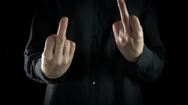 Show disrespect gesture against black background. A view of man with angry emotions show middle finger gesture indoor.