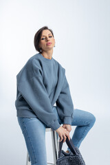 Beautiful woman of model appearance. Girl in grey sweatshirt with black bag on light background....