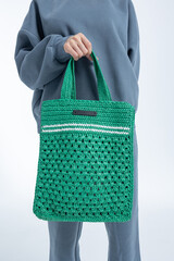 Beautiful woman of model appearance. Girl in grey sweatshirt with green bag on light background....