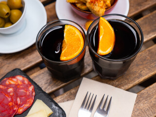 Aromatized sweet red vermouth garnished with orange slices served in two glasses with chorizo, cheese and olives. Traditional Spanish vermouth hour