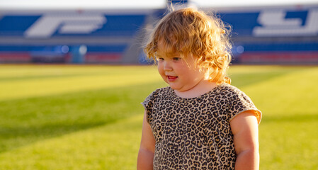 Young child dressed in a playful leopard print outfit is walking barefoot across a lush green lawn...