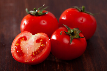 Closeup of whole and halved fresh organic tomatoes on wooden surface. Healthy vegetarian ingredient