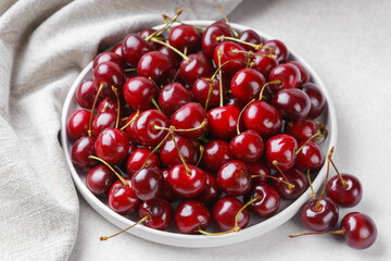 Close up of white plate filled with ripe red sweet cherry placed on gray linen napkin on light...
