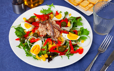 Lettuce, corn, olive, anchovy, boiled egg salad served on table with serving pieces.