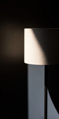 A floor lamp turned on near a wall in a dark room. Warm light creates soft shadows and a cozy ambiance. Minimalist interior in Scandinavian style.