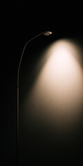 A floor lamp turned on near a wall in a dark room. Warm light creates soft shadows and a cozy ambiance. Minimalist interior in Scandinavian style.