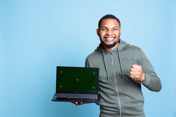 Young friendly african american guy feeling positive next to copy space mockup, gesturing for an advertisement against blue background. Male model with a hoodie smiling in studio.
