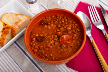 Delicious hearty stew of lentils with meat, smoked pork chorizo sausage and vegetables served in clay bowl. Authentic Spanish dish