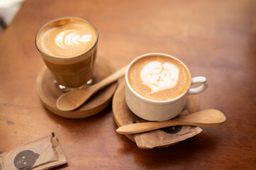 Two Coffee Cups with Latte Art in Steam on Wooden Tabletop with Wooden Spoons