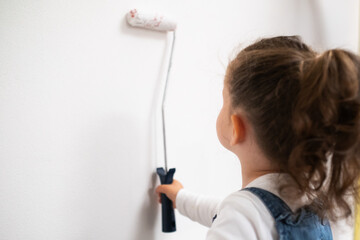 Creative toddler girl paints a wall in the apartment, home activity and family life concept.