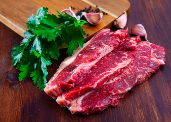 Fresh raw sliced marbled beef meat with parsley and condiments prepared for roasting on wooden table