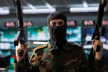 Obraz premium Portrait of dangerous masked terrorist holding assault rifles able to engage targets at extended range with accurate, lethal fire. Insurgent using guns, assaulting enemy base during guerilla war