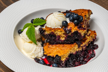 White plate with piece of fresh baked blueberry cobbler and ice cream on wooden background, closeup. Homemade berry cobbler ready to eat