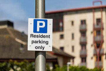 Close-up of a 'Resident parking only' sign on a post. The blurred residential building in the...