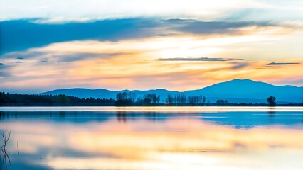 A tranquil lake reflecting a vibrant sunset with distant mountains and trees line