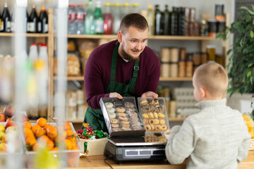 Friendly salesman kindly assisting little boy purchasing cookies in grocery store