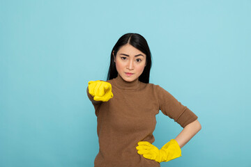 Frustrated female cleaner in yellow rubber gloves pointing finger directly at camera, expressing...
