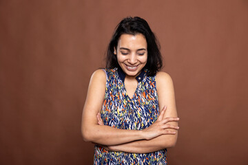 Beautiful Indian woman laughing uncontrollably with head bowed down, standing against brown...