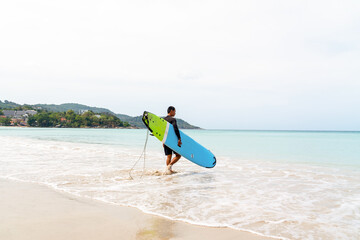 Confidence Asian man in sportswear enjoy water sports surfing at the sea on summer beach holiday vacation. Healthy people outdoor active lifestyle holding surfboard walking on the beach in sunny day.