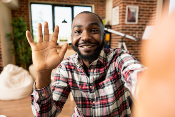 Happy bearded black man waves at camera, connecting remotely with colleague in modern apartment...
