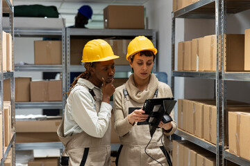 Multiethnic staff scanning goods on warehouse shelving unit to manage inventory and stock delivery....
