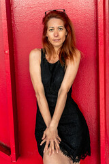 Redhead woman posing with black dress against red wall