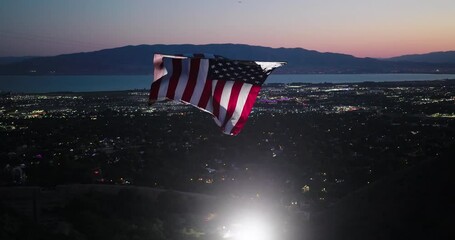 Glowing, giant American flag flying over sparkling valley and distant lake at dusk