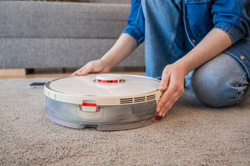 side view on woman turning on robot vacuum cleaner. smart home concept 