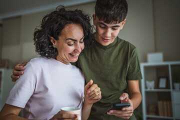 mother and young son teenage boy use mobile phone together at home