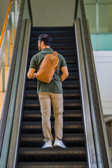 A man carrying a light brown leather shoulder bag is standing on an escalator, perfect for a leather products catalog design.