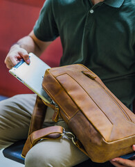 A man's hand puts a gadget into a brown leather sling bag, perfect for a leather product catalog design.