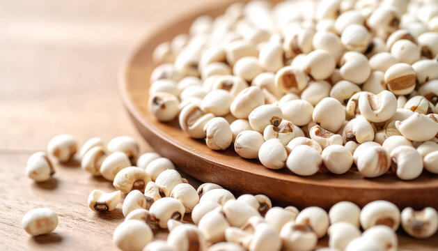 A close-up view of uncooked Job's Tears scattered on a wooden plate.